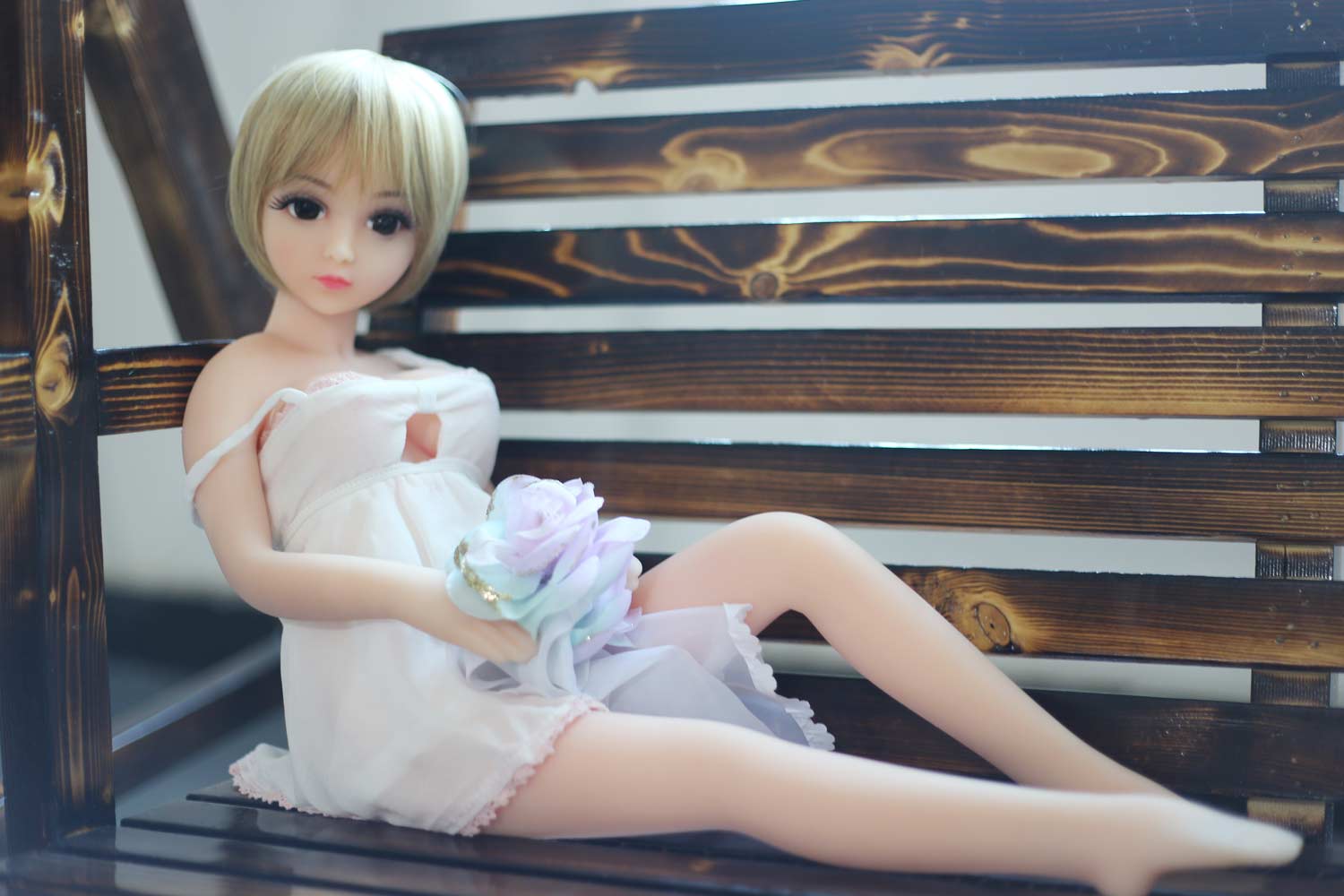 A mini sex doll sitting on a chair with a flower in the hand