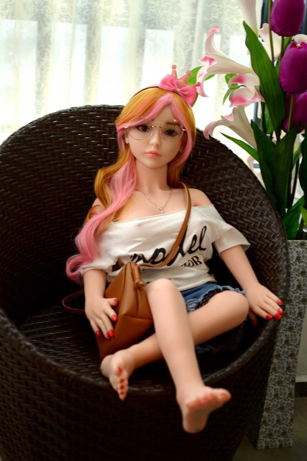 A mini sex doll with glasses sitting on a chair