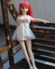 Mini sex doll with red long hair standing on a chair