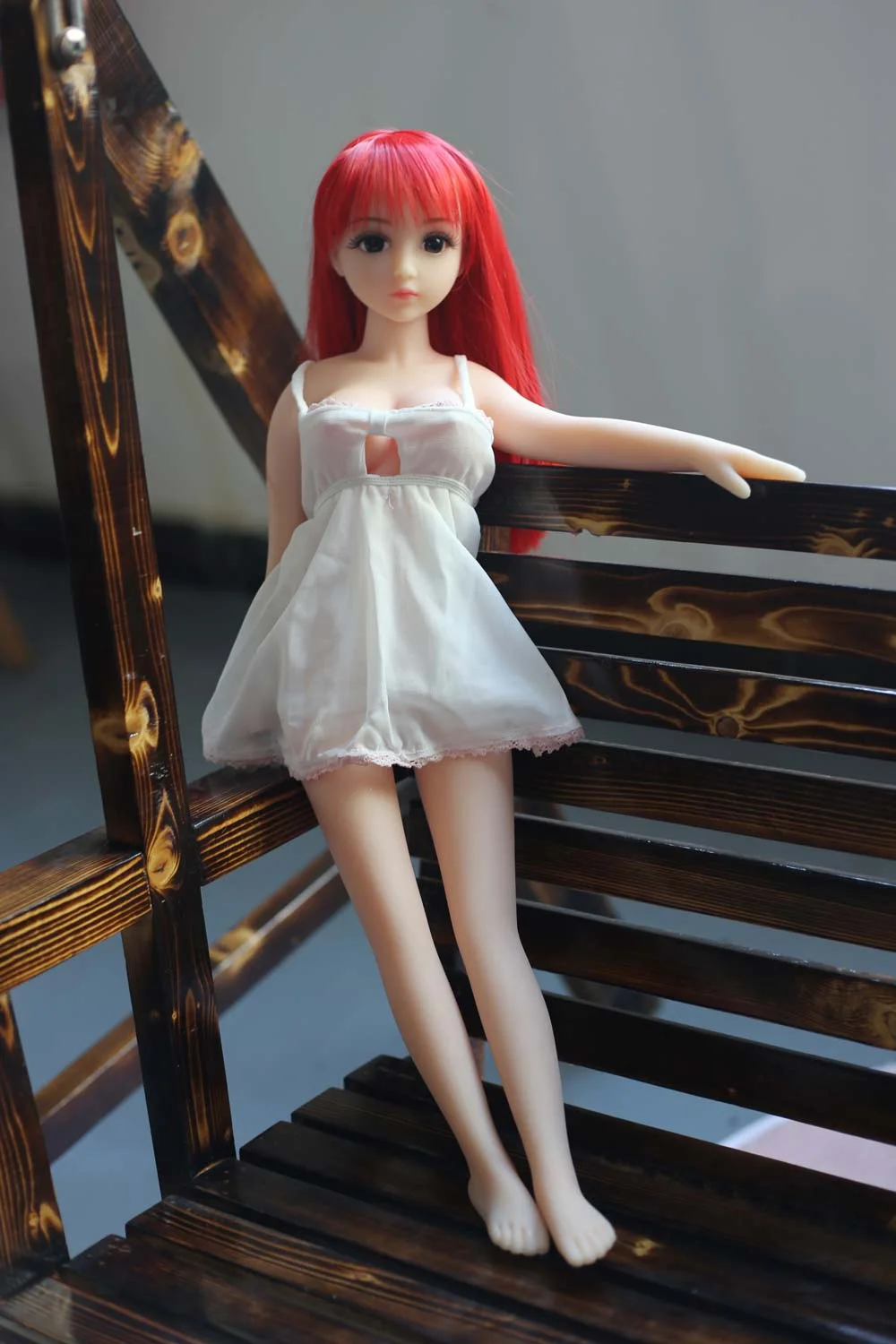 Mini sex doll with red long hair standing on a chair