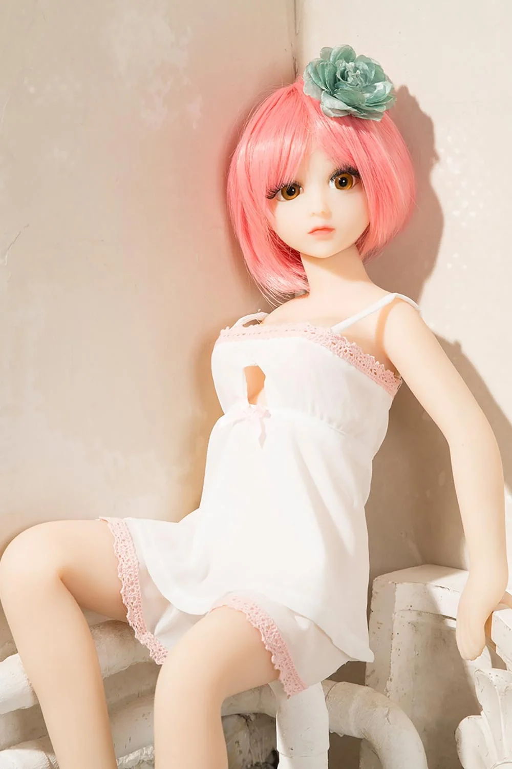 Mini sex doll with short pink hair leaning against the wall