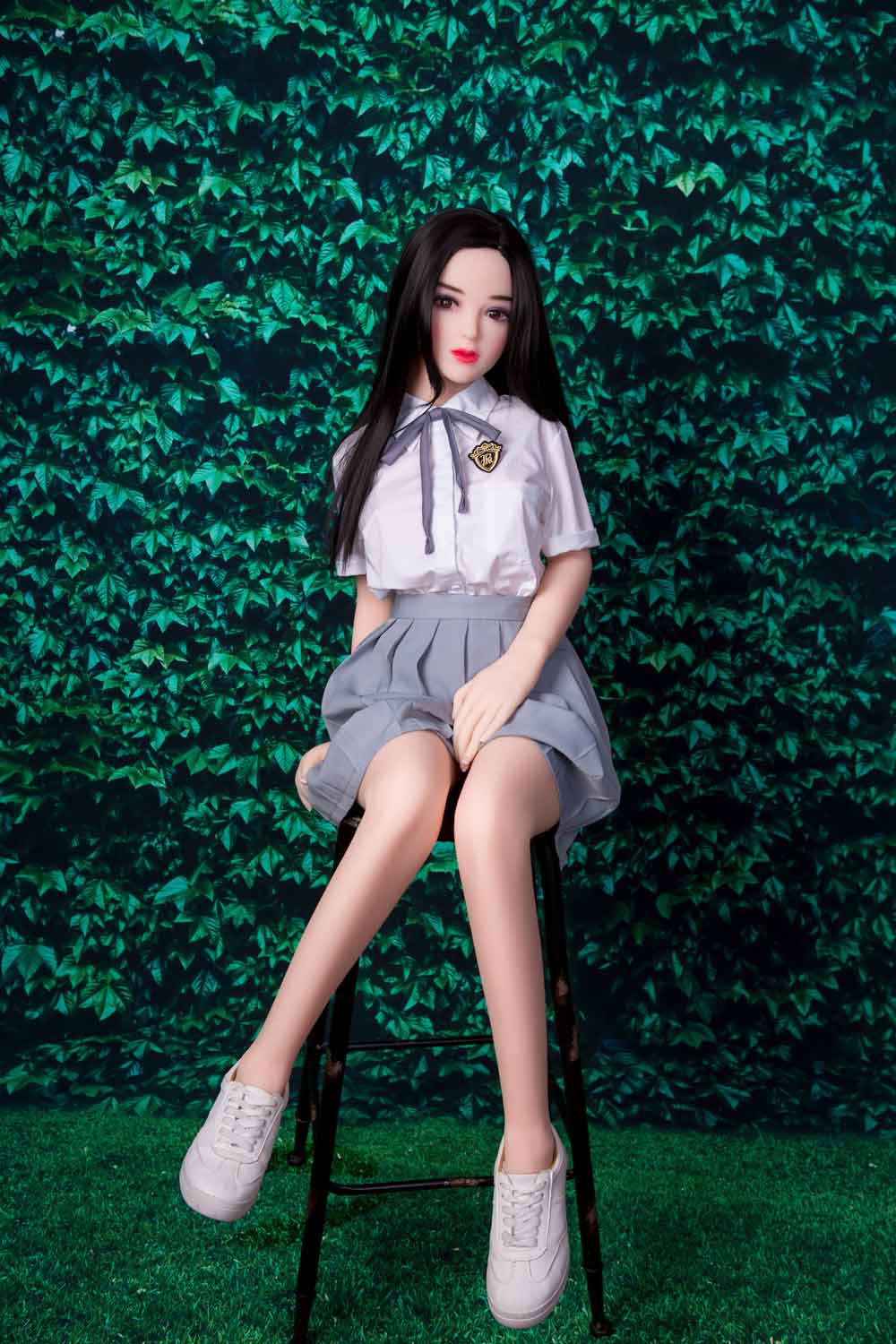 A mini sex doll sitting on a stool with hands between thighs