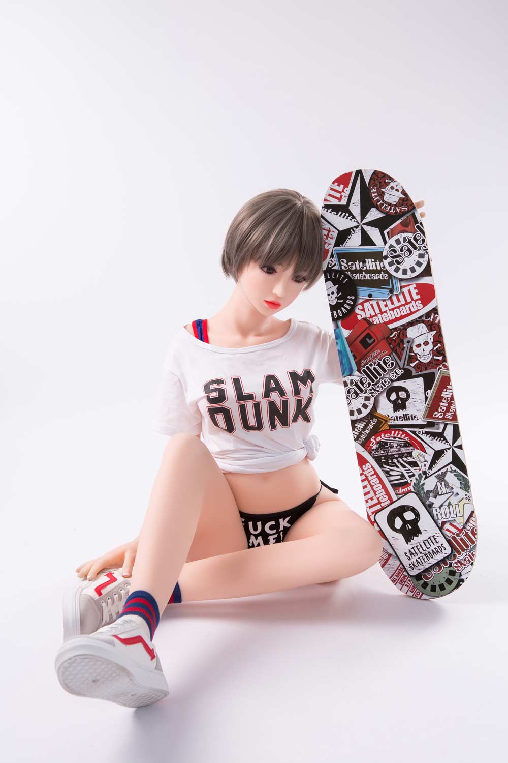 A mini sex doll sitting on the ground holding a skateboard
