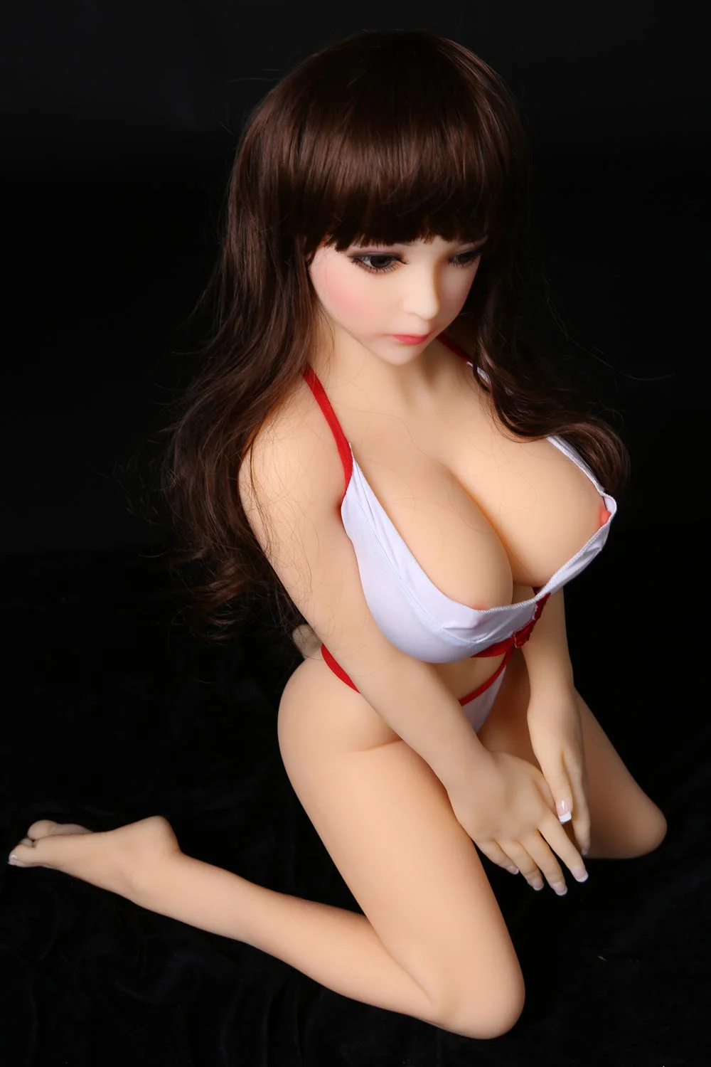 A mini sex doll with knees on the ground and hands between thighs