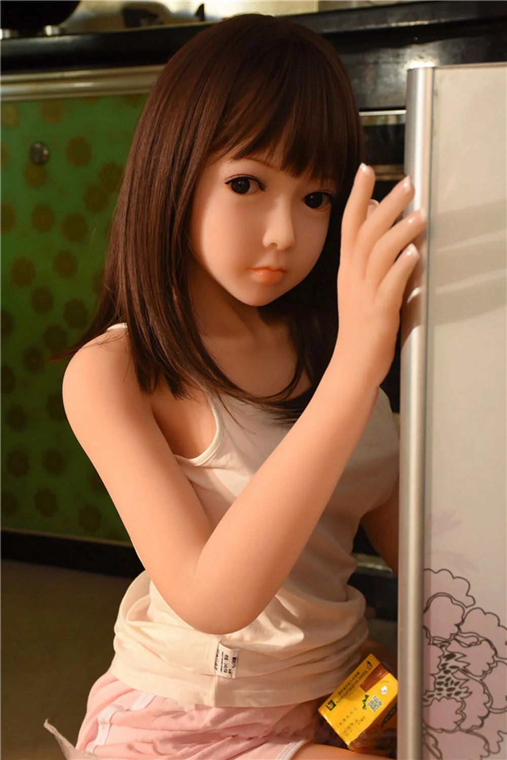 A sex doll kneeling on the floor with hands on the cupboard
