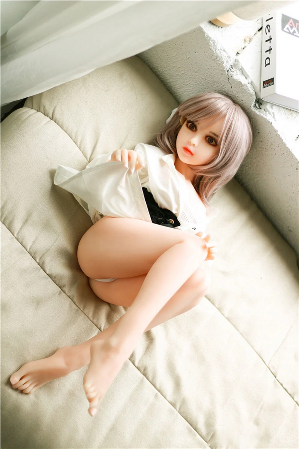 Mini sex doll lying on the bed with legs bent