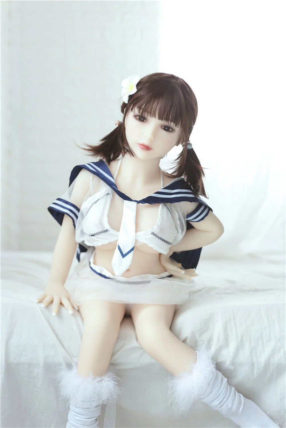 Mini sex doll sitting on the side of the bed with hands on waist